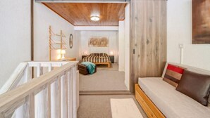 A cozy room with a wooden ceiling, a bed with a striped blanket, a sofa with a brown cushion, and a wooden railing. - Les Genepis (Val Claret) by Interhome (Tignes)