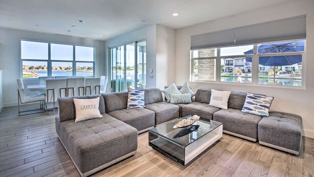 A modern living room with a sectional sofa, a glass coffee table, and large windows offering a view of the pool and outdoor area.