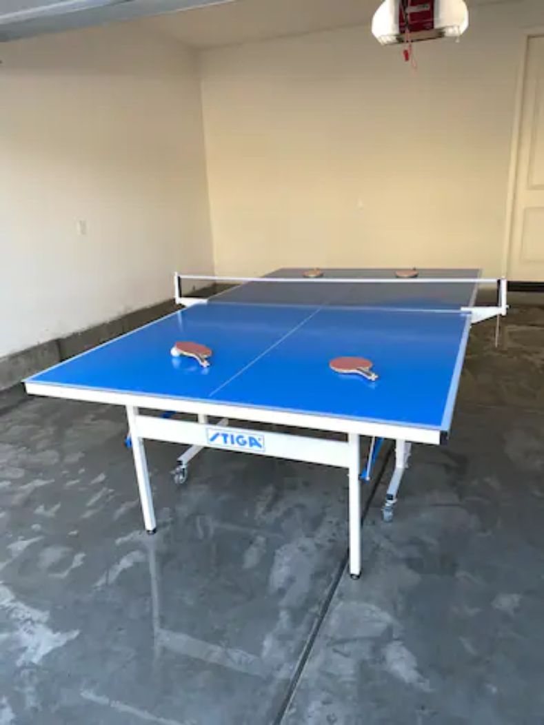 A ping pong table with two paddles in a room with a concrete floor and a white door in the background.