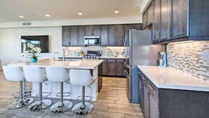 A modern kitchen with dark cabinets, a central island with bar stools, and a microwave above the island.