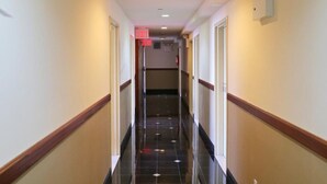 Um corredor de hotel com piso preto polido, paredes brancas e detalhes em madeira.