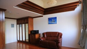 Um quarto amplo com piso de madeira, uma poltrona de couro, uma televisão em um armário de madeira e um quadro na parede.