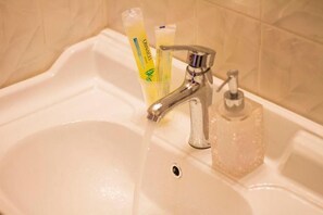 A bathroom sink with a chrome faucet, a soap dispenser, and two toothbrushes in a transparent container. - Phoenix Hotel (Brooklyn)
