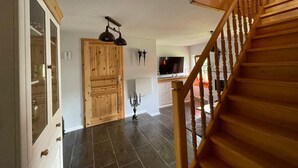 Una escalera de madera conduce a un espacio de estar con televisor, una puerta de madera y un mueble con puertas de cristal.