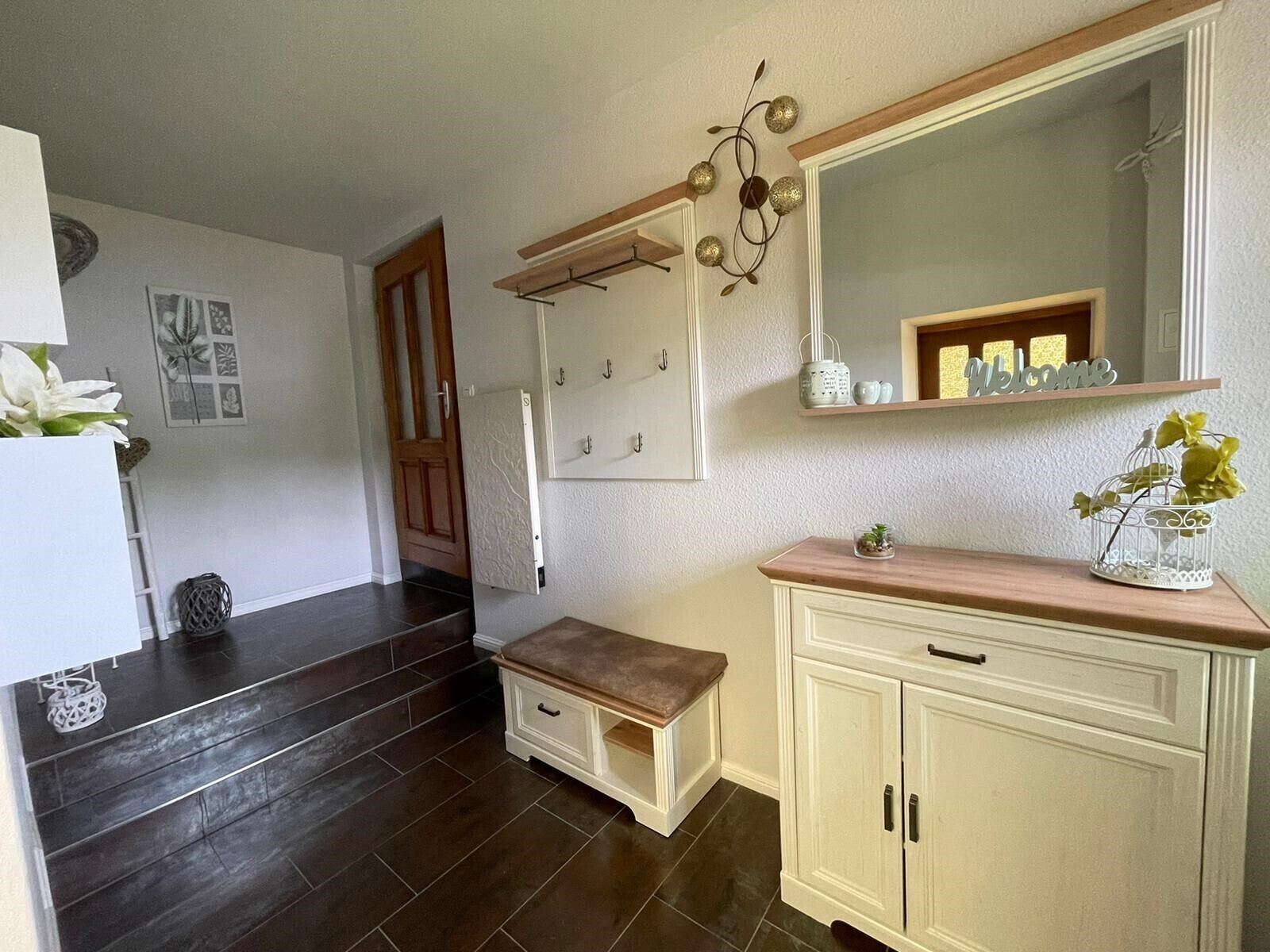 A hallway with a wooden bench, a white cabinet with drawers, a large mirror, and a wall-mounted light fixture.