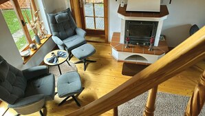 Una sala de estar acogedora con chimenea, piso de madera y vistas al jardín a través de amplios ventanales.