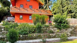 Una casa de dos pisos con fachada roja, un balcón y un muro de piedra al frente.
