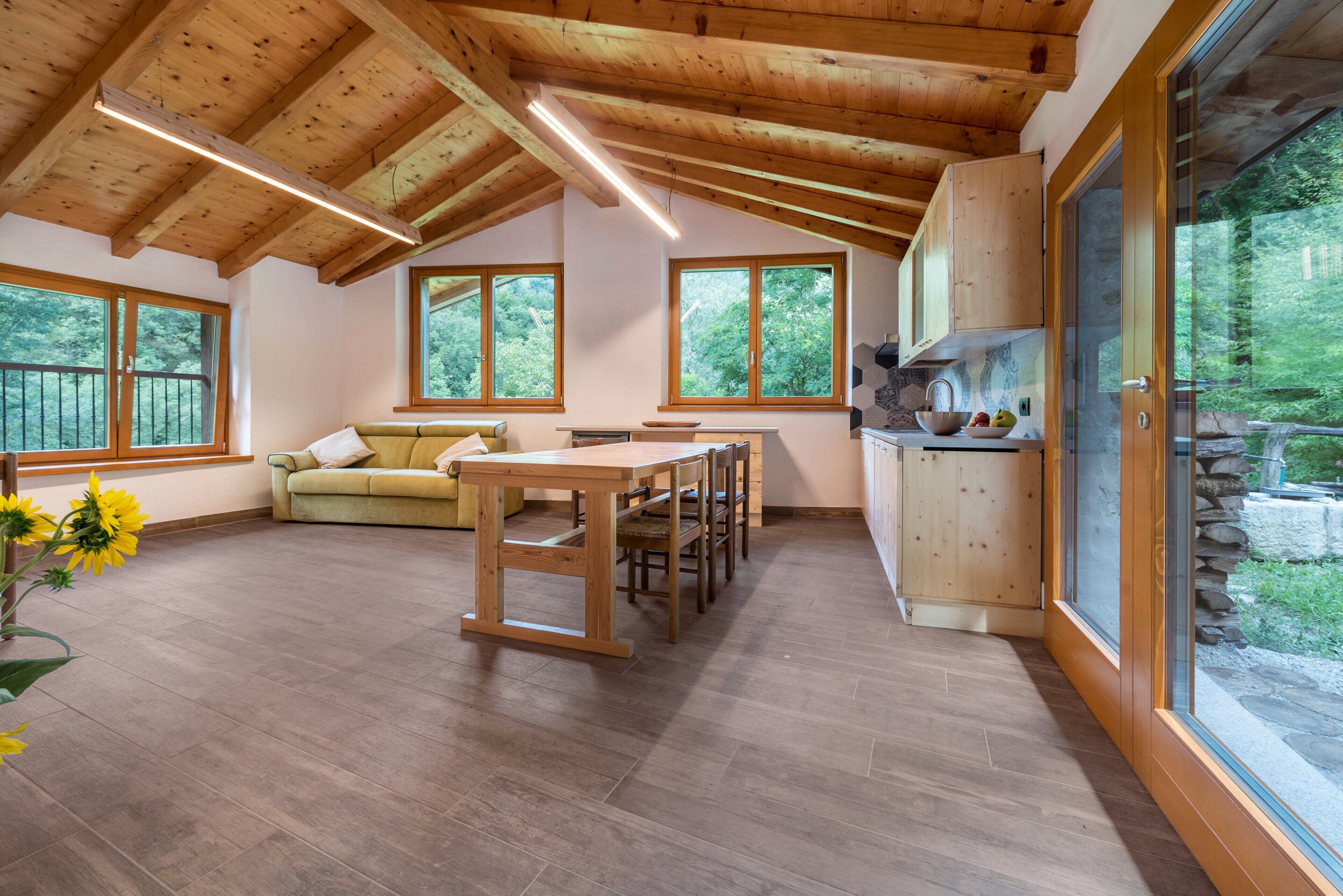 A spacious room with a wooden ceiling, large windows, a dining table, and a sofa.