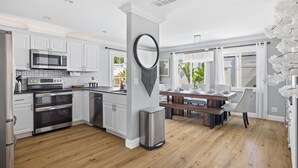 A modern kitchen with stainless steel appliances, a dining area with a wooden table, and a large window with white curtains. - Laguna vacation home pool Sauna jacuzzi (Laguna Hills)