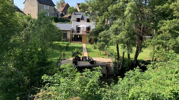 Et hus med facade af sten, træterrasse og et lille vandelement i haven.