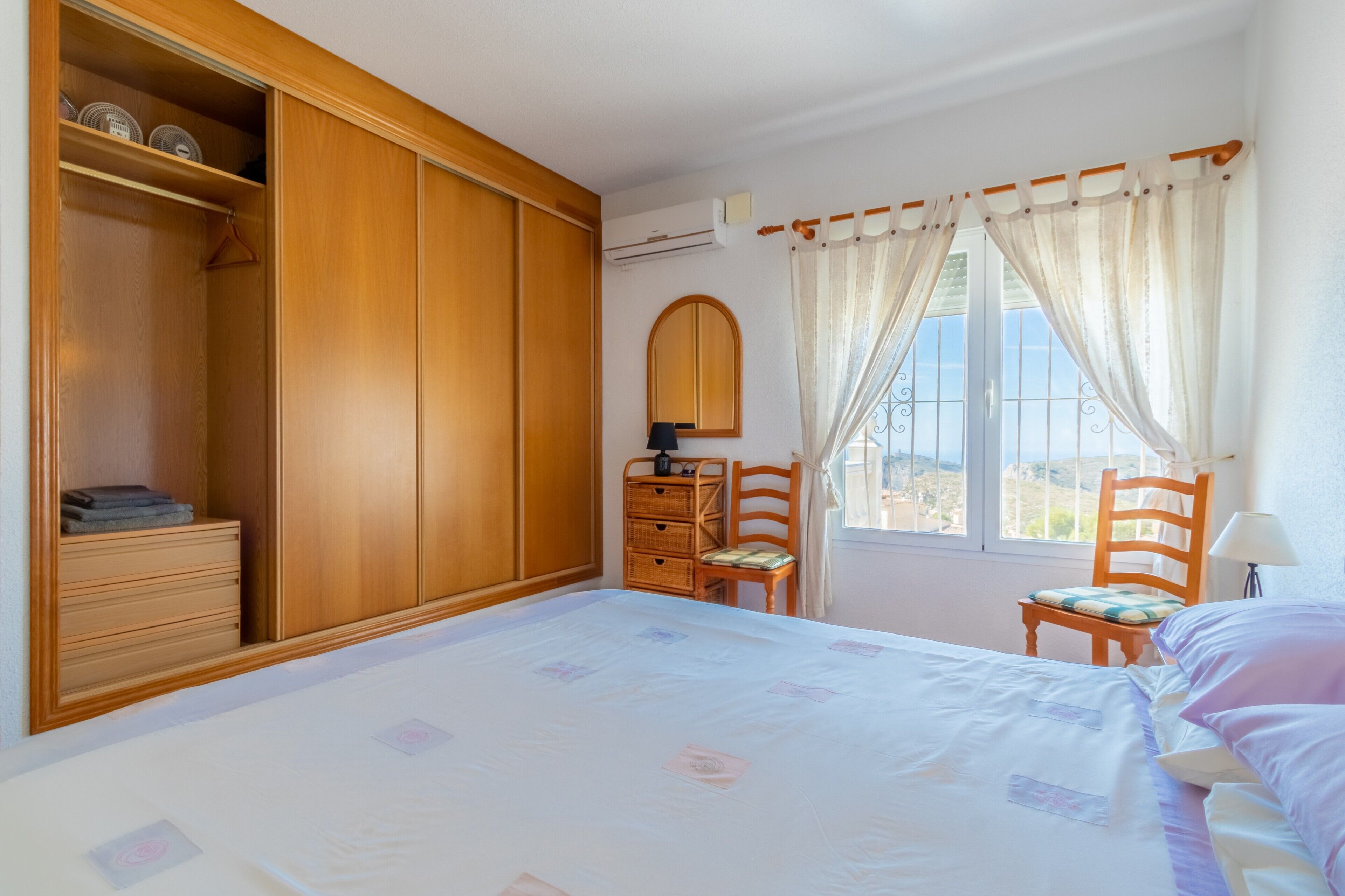 Une chambre à coucher avec un grand lit, une armoire en bois, une chaise, un bureau et une fenêtre avec des rideaux.
