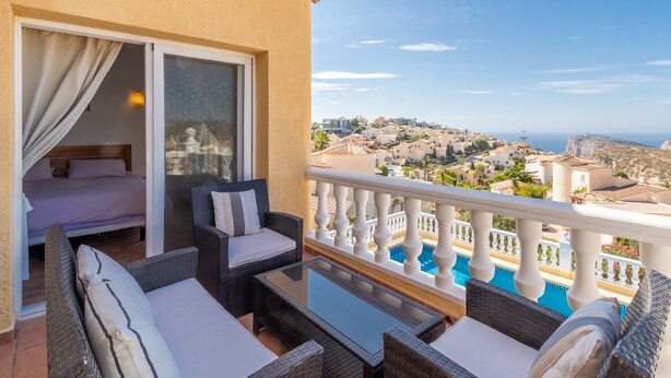 Ein Balkon mit einem Bett, Korbmöbeln, einem Glastisch und Blick auf einen Pool.