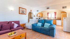 Ein Wohnzimmer mit einer Couch, einem Esstisch und einer Küchenzeile inklusive Kühlschrank und Schränken.