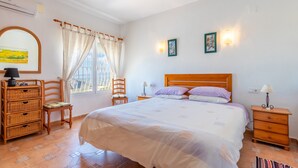 Ein Schlafzimmer mit Bett, Stuhl, Kommode, Nachttisch und einem Fenster mit Vorhängen.