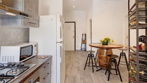 Une cuisine moderne équipée d’une cuisinière à gaz, d’un four à micro-ondes, d’un réfrigérateur et d’une table ronde en bois, accompagnée de tabourets.