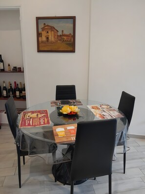 Una mesa redonda de vidrio con un centro de flores, rodeada de sillas negras, en una habitación con pared blanca y un cuadro enmarcado.