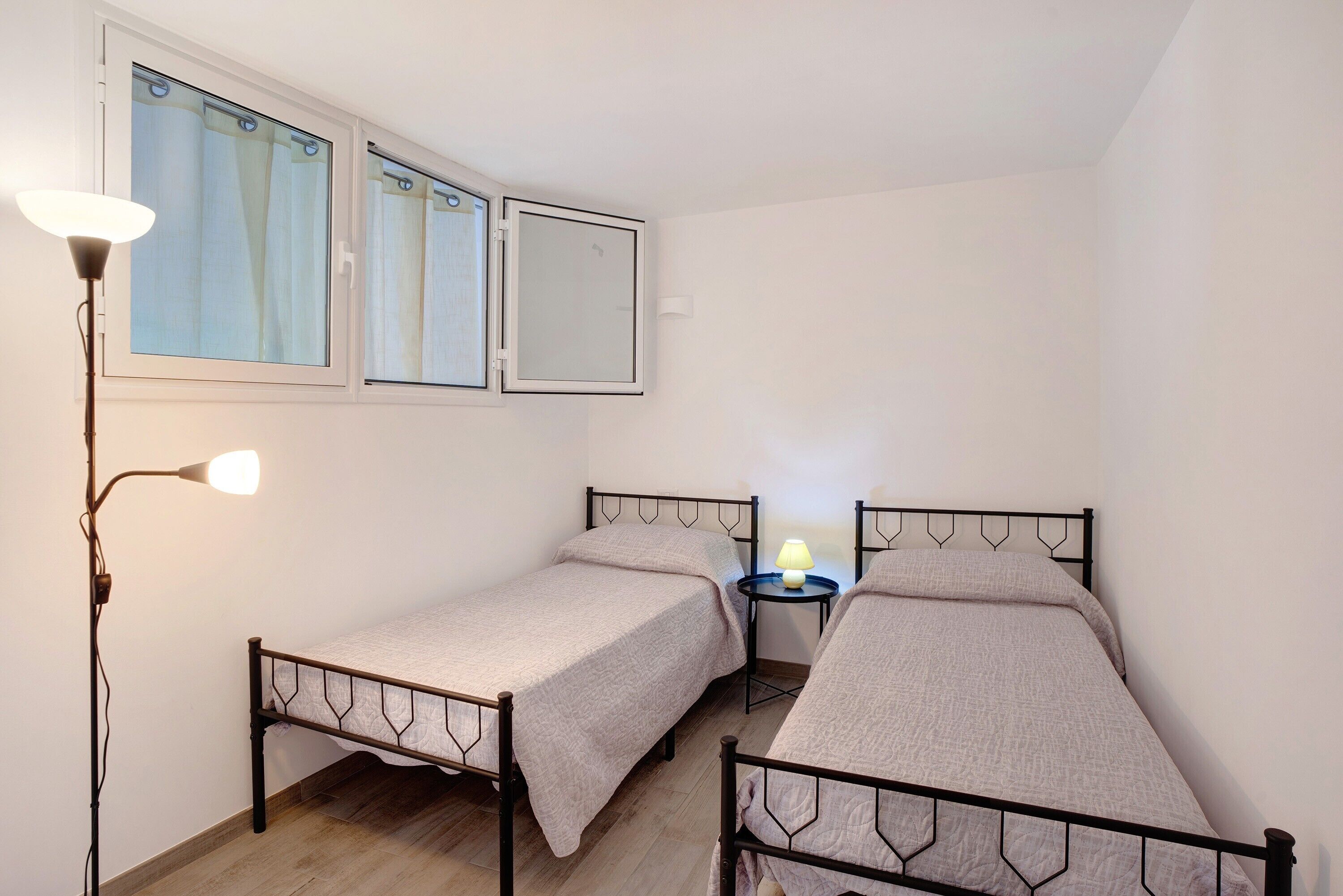 Une petite chambre avec deux lits simples, une table de chevet avec une lampe et une fenêtre avec des rideaux.
