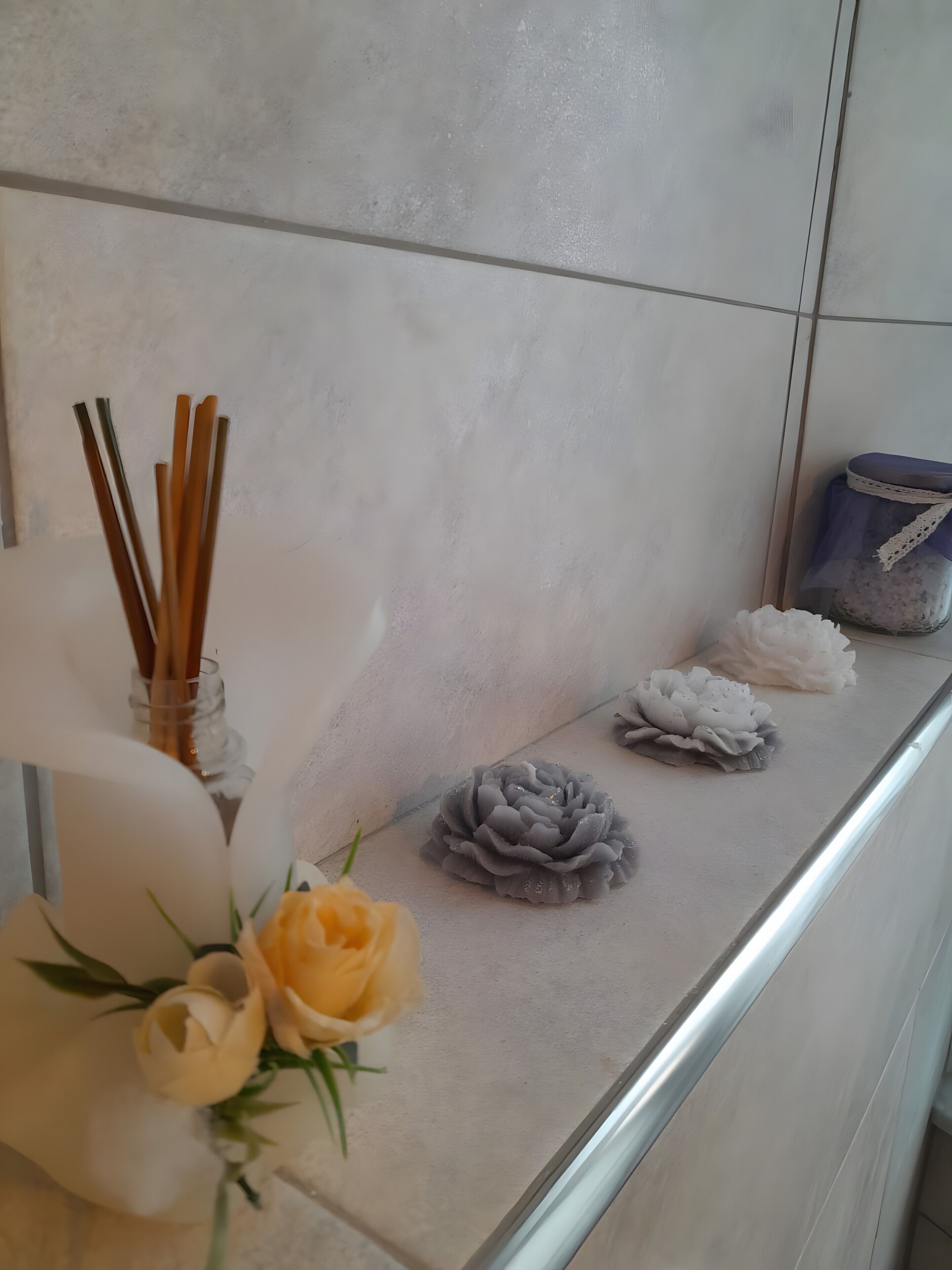 A bathroom with a white sink, a glass jar with a white cloth, and a vase with yellow flowers.