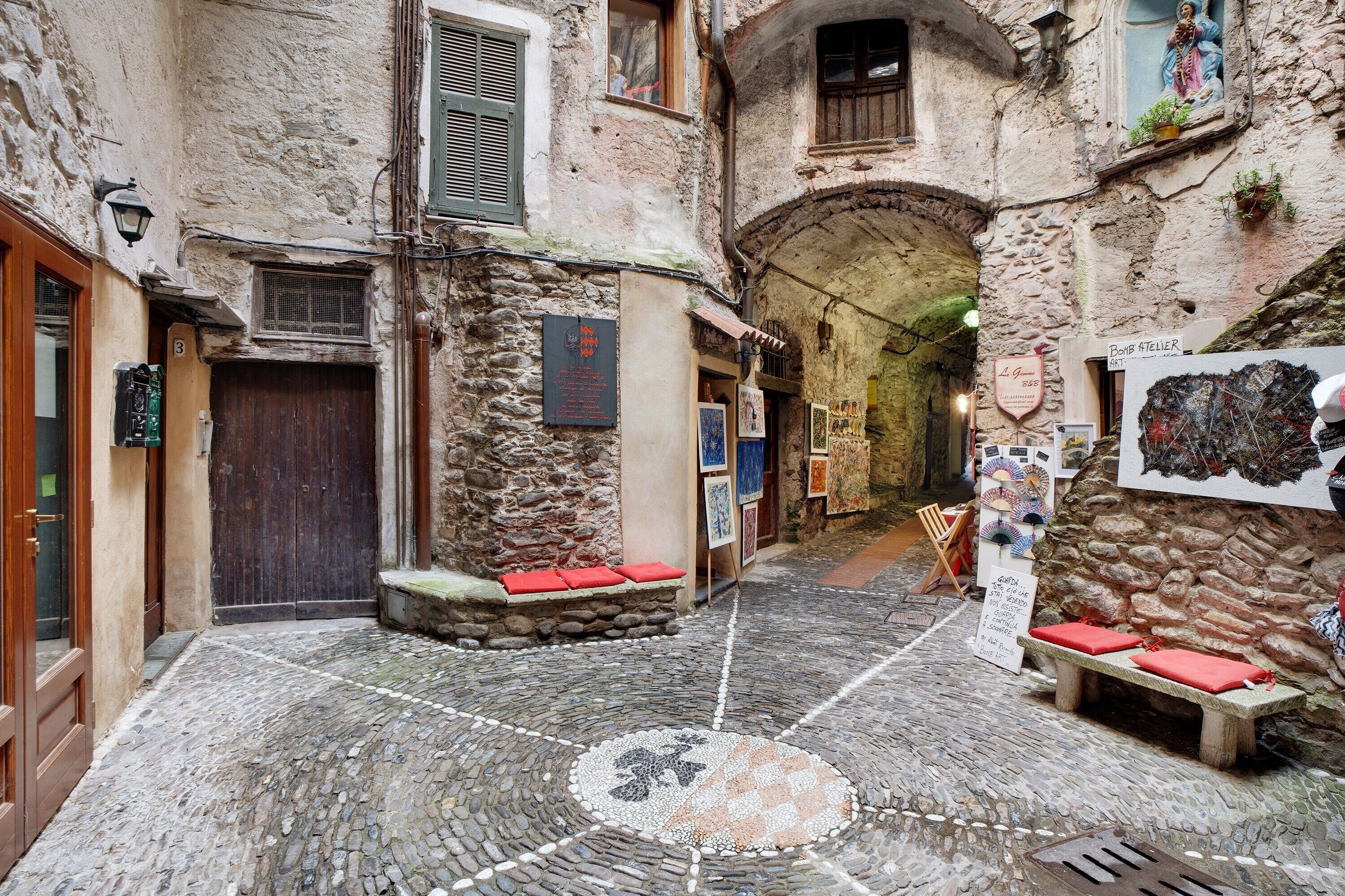 A cobblestone courtyard with stone benches, a wooden door, and a stone wall with artwork.