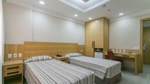 Quarto de hotel com duas camas, uma escrivaninha, uma cadeira e um guarda-roupa.