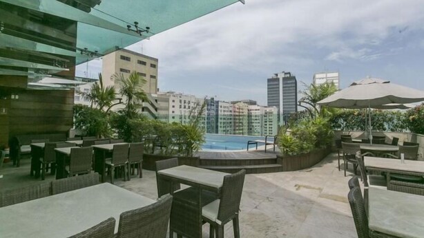 Uma área de varanda externa com mesas e cadeiras, piscina e vista para a cidade.