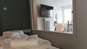 Habitación de hotel con cama, televisión montada en la pared, una kitchenette pequeña y vistas al comedor a través de una ventana.