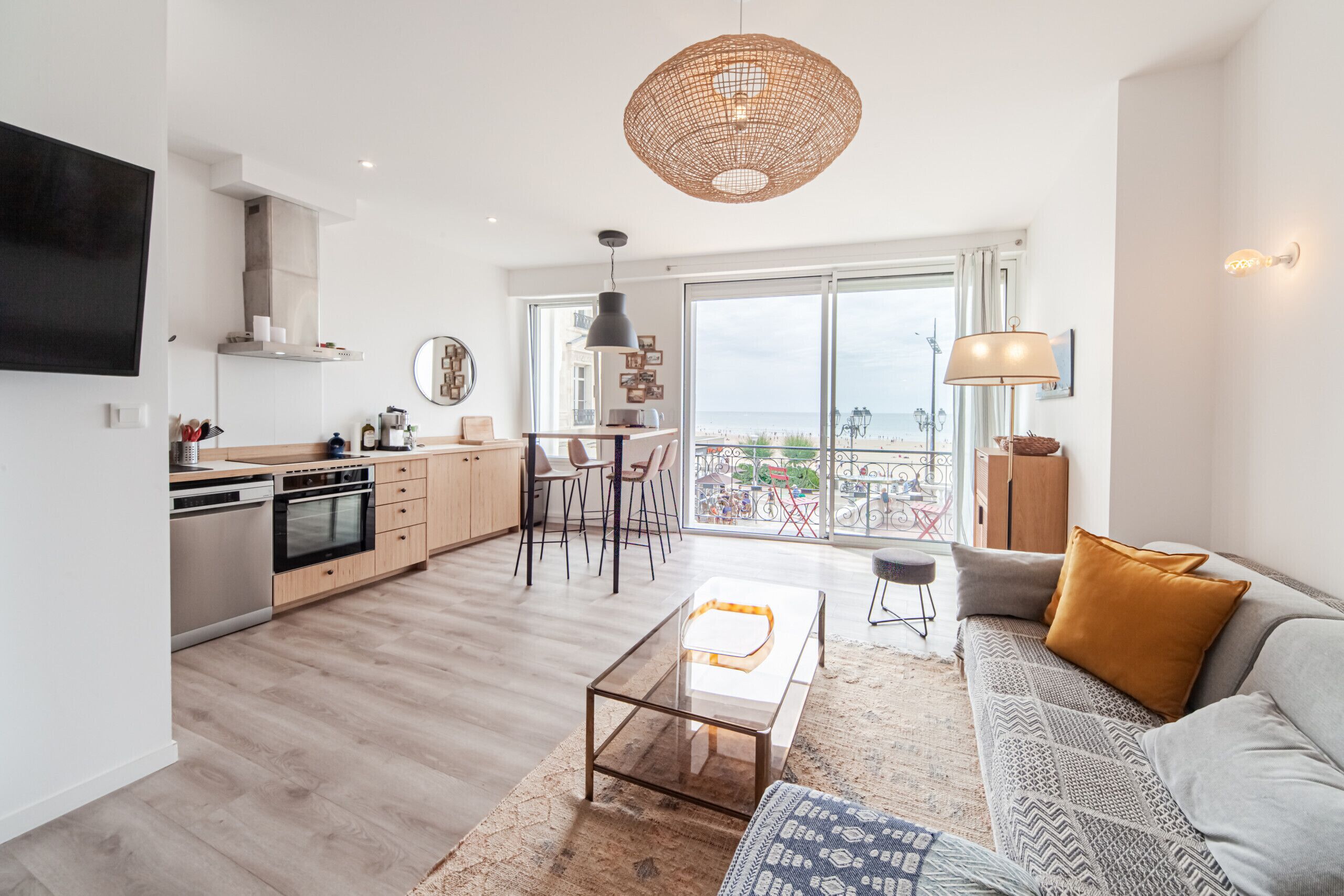 A modern apartment with a kitchen, dining area, and living room. It features a large balcony with a view of the beach.
