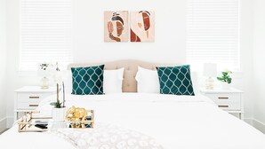 A neatly arranged bedroom with a large bed, two nightstands, a bedside table, and a window with blinds.