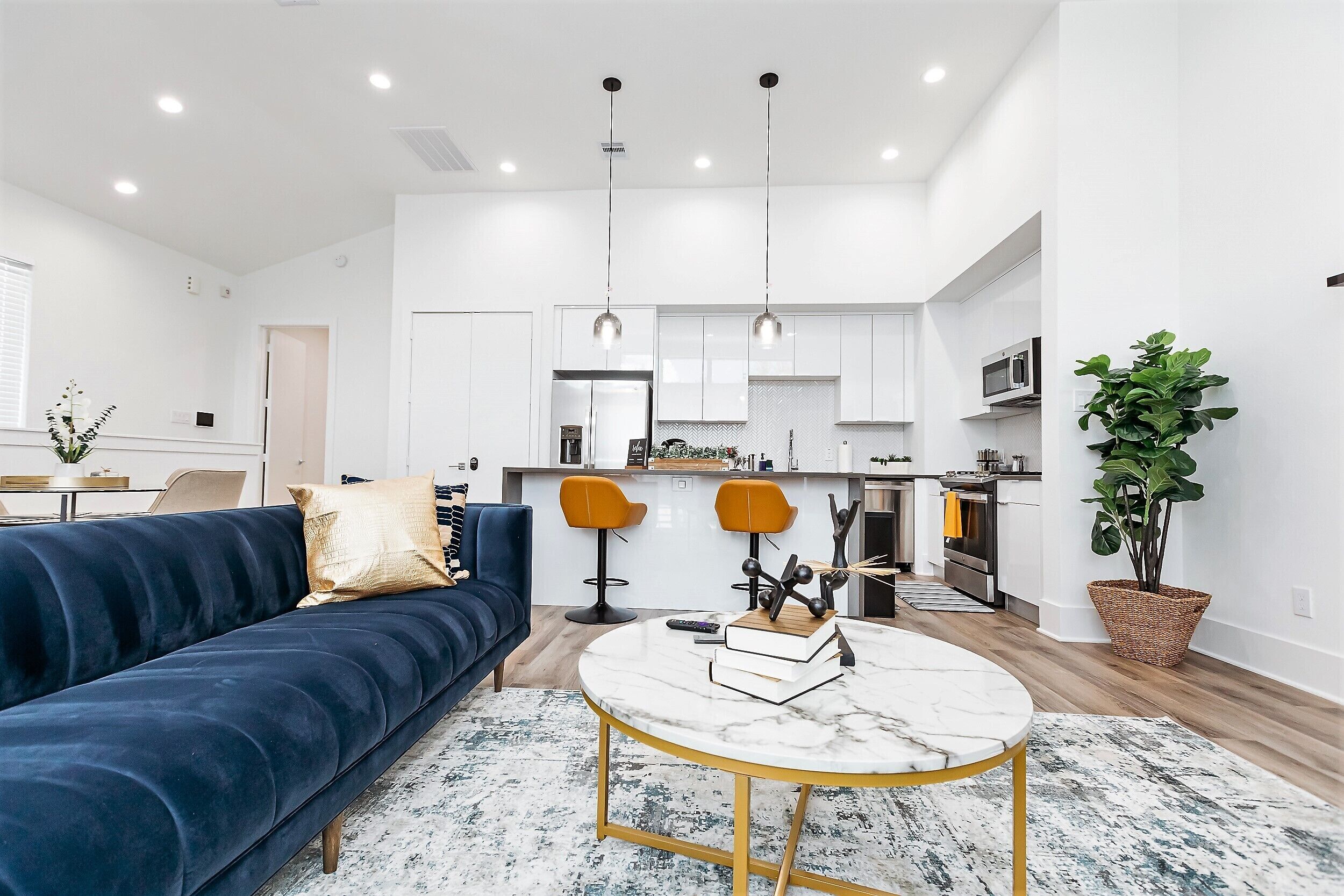 A modern living room with a dark blue sofa, a round marble coffee table, and a kitchen in the background.