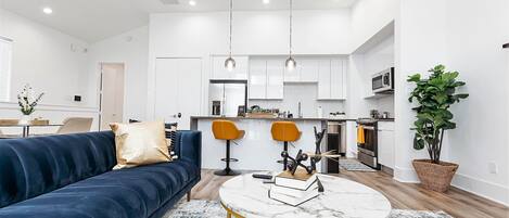 A modern living room with a dark blue sofa, a round marble coffee table, and a kitchen in the background.