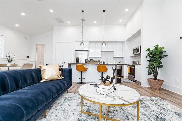 A modern living room with a dark blue sofa, a round marble coffee table, and a kitchen in the background.