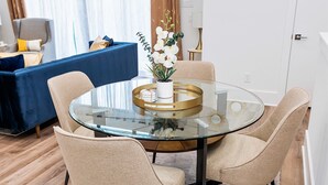 A modern dining area with a glass table surrounded by beige chairs, a potted orchid, and a blue sofa in the background.