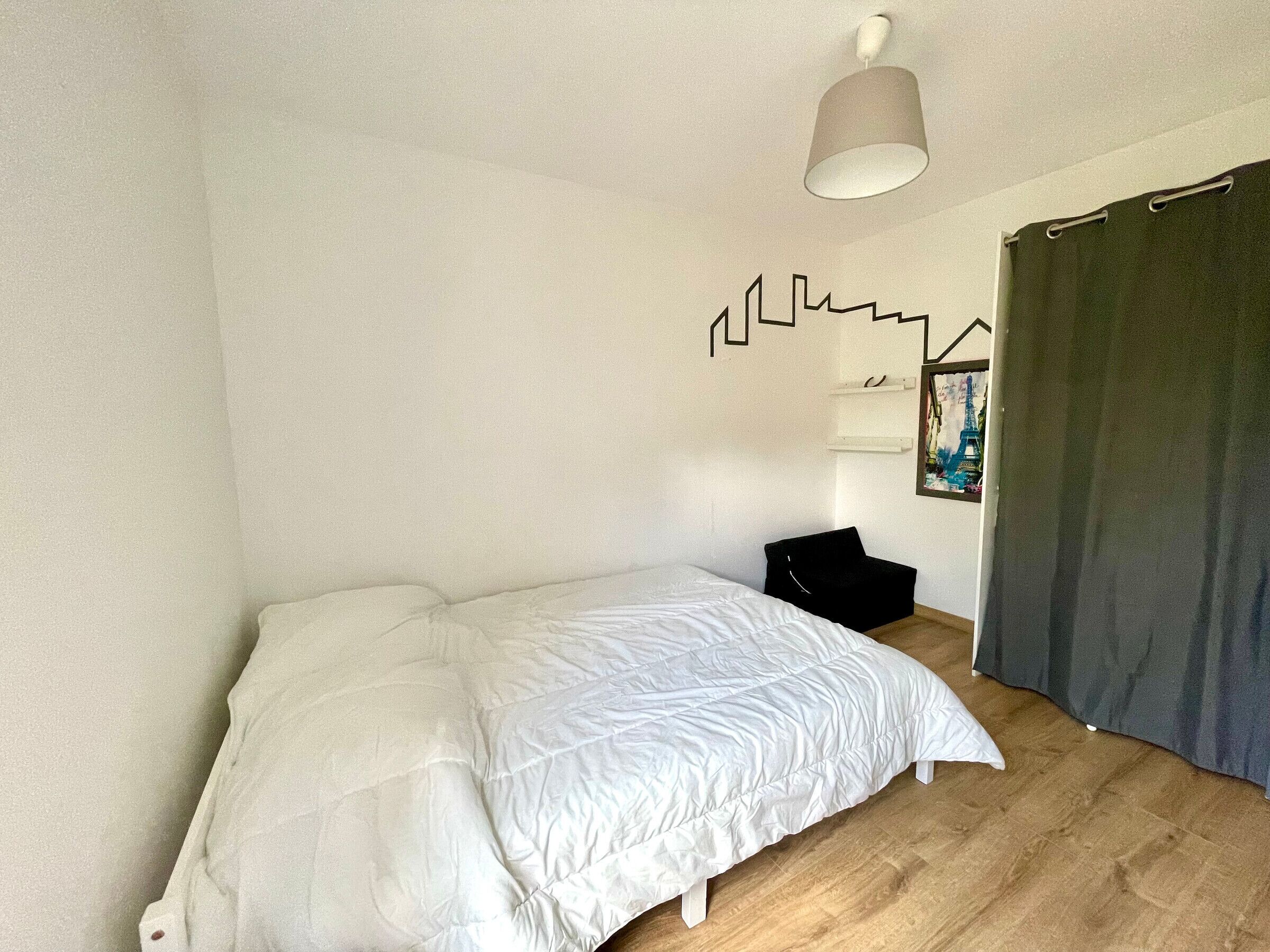 A bedroom with a bed, a hanging lamp, a picture frame, and a curtain.
