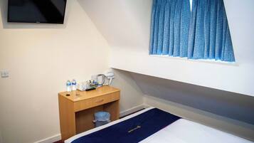 A hotel room with a bed, a desk with a mirror, a TV mounted on the wall, and a window with curtains.