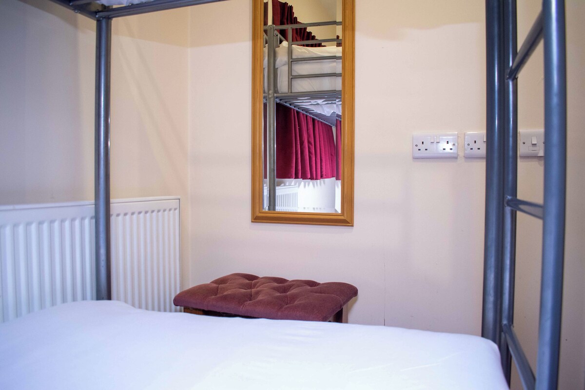 A bunk bed with a window, a radiator, and a power outlet on the wall.