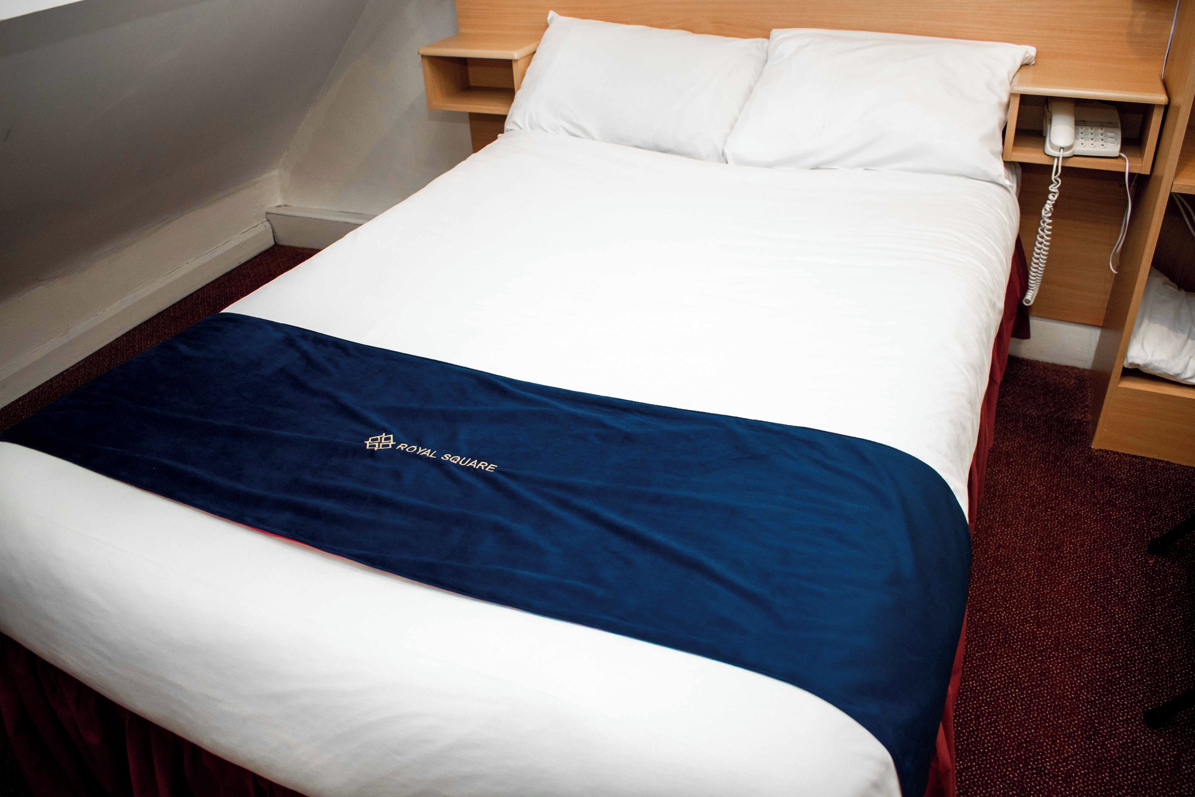 A hotel room with a bed, a bedside telephone, and a wooden nightstand.