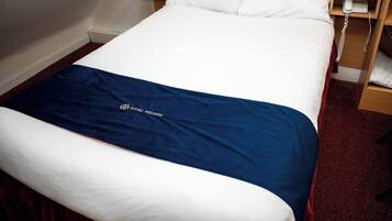 A hotel room with a bed, a bedside telephone, and a wooden nightstand.