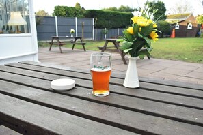 A glass of beer on a wooden table with a white lid beside it, and a white vase with yellow flowers in the background. - Royal Square Hotel - NEC and Birmingham Airport (Birmingham)