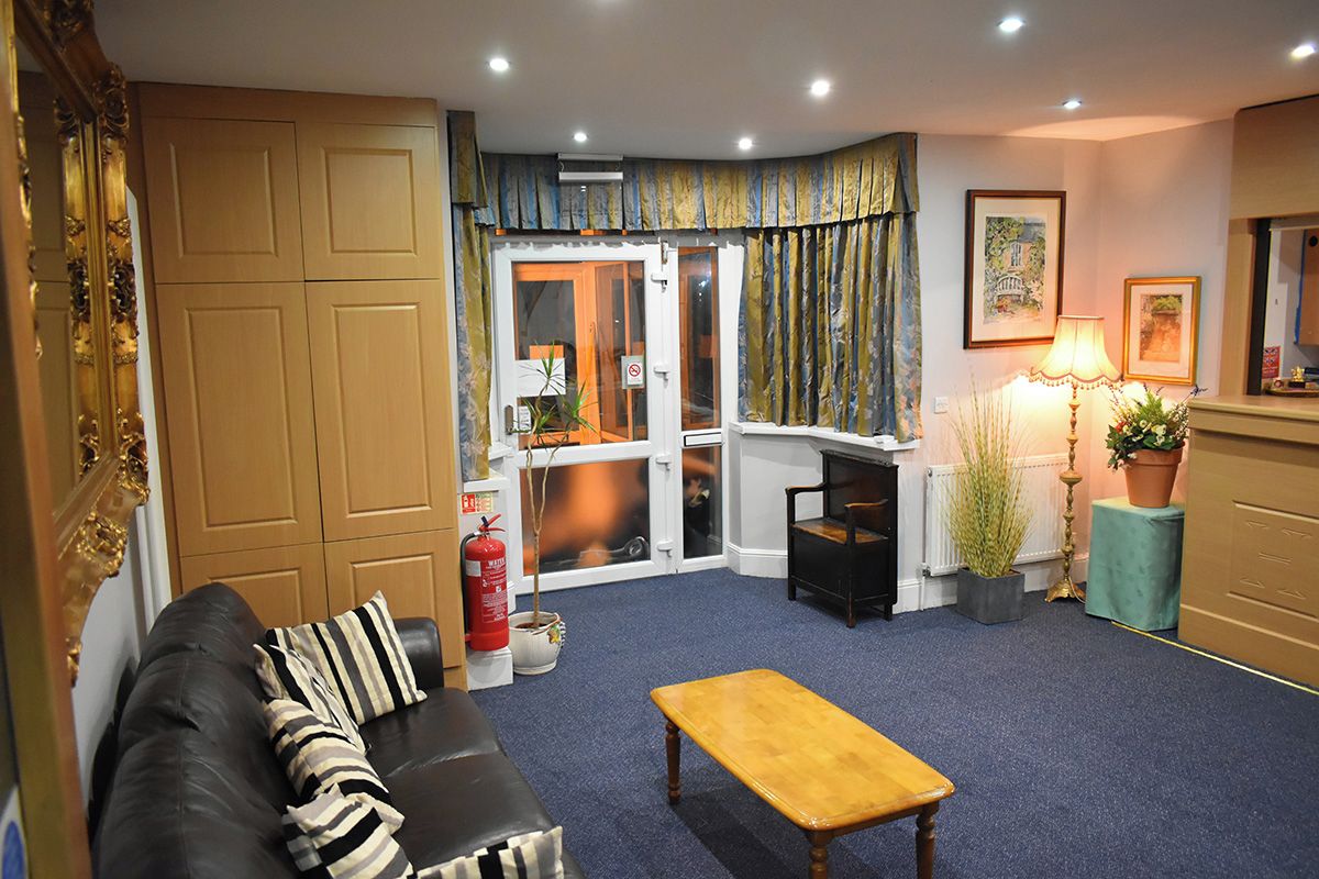 A hotel lobby with a sofa, a wooden table, a fire extinguisher, a potted plant, and a framed picture on the wall.