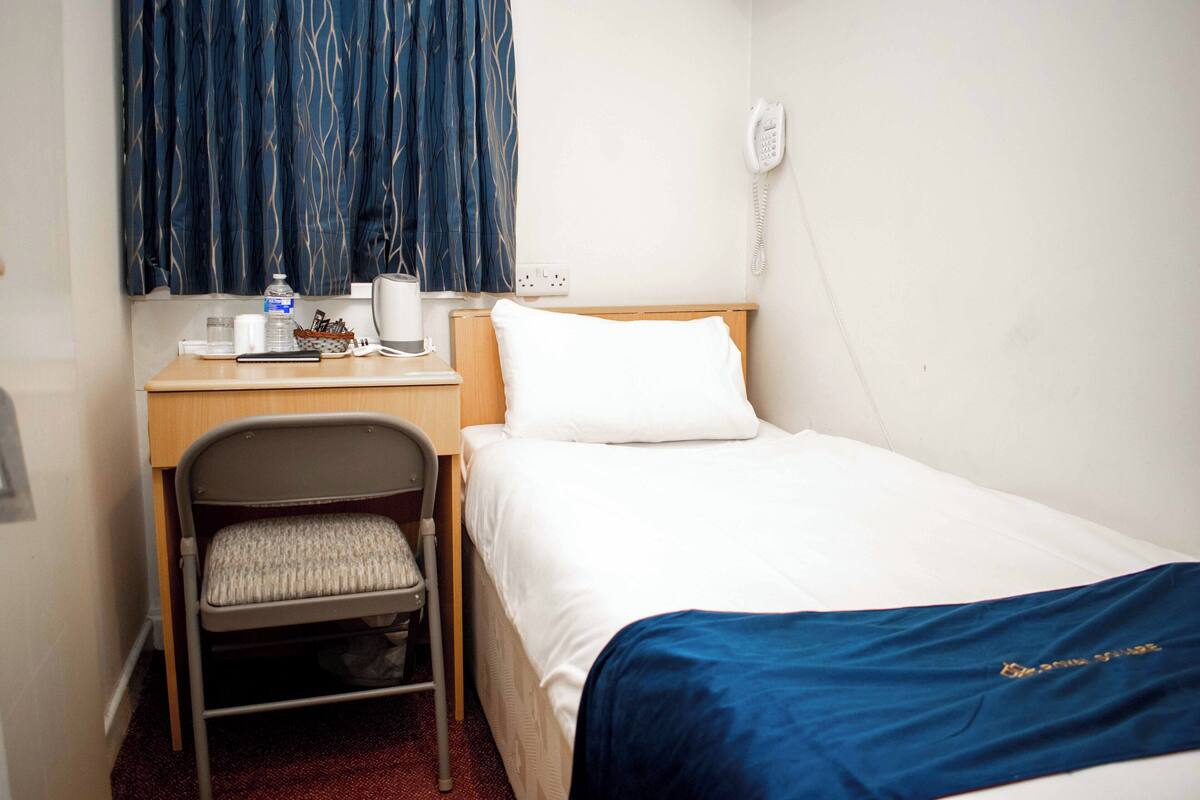Une chambre d’hôtel avec un lit, un bureau et une chaise, un téléphone et une fenêtre avec des rideaux.