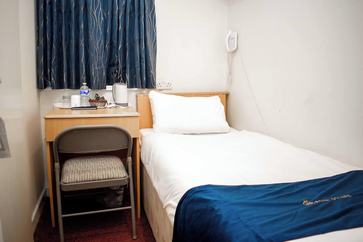 A hotel room with a bed, a desk with a chair, a telephone, and a window with curtains.