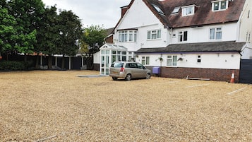A residential property with a car parked in front, a gravel driveway, and a white house with a red roof.