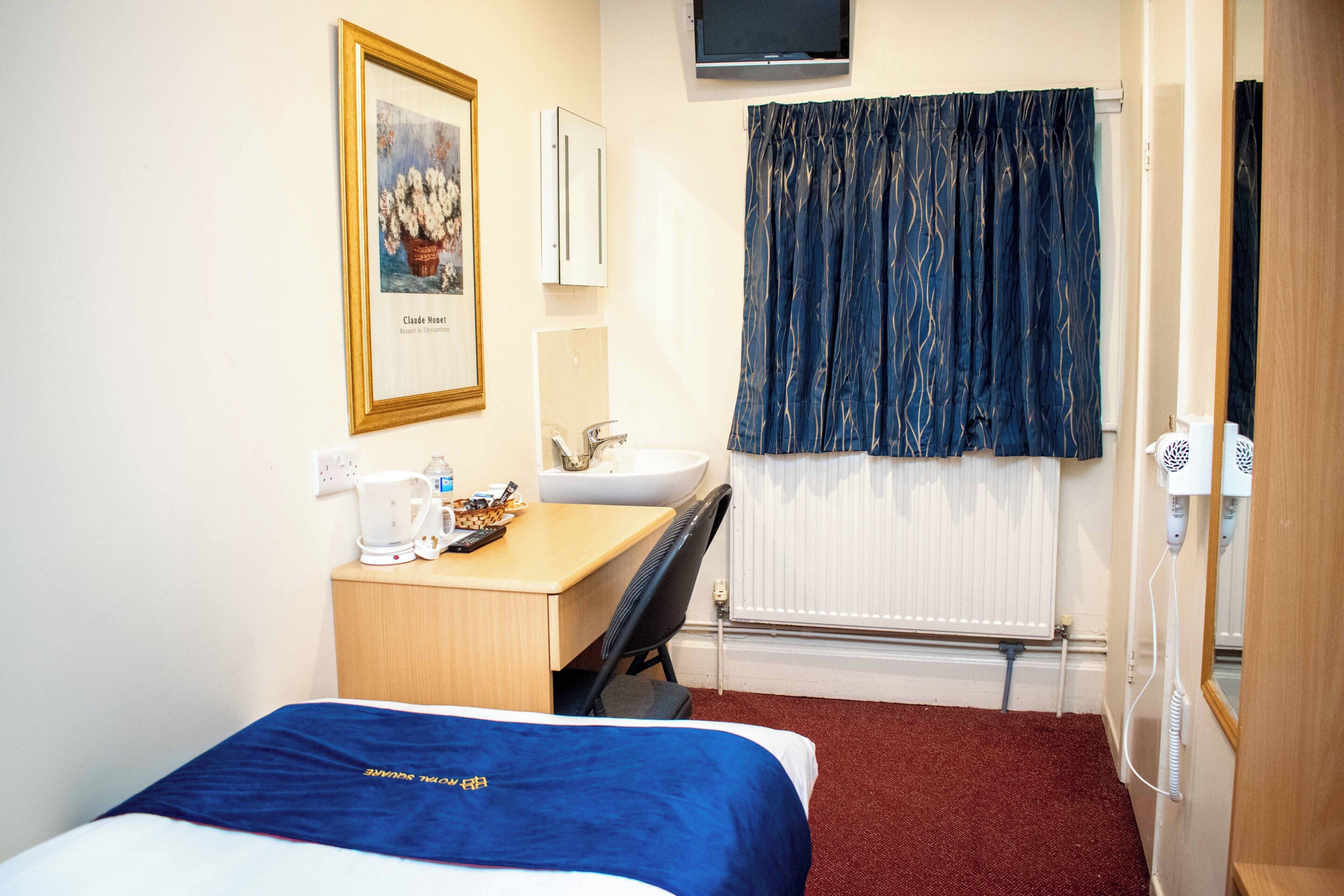 Hotelkamer met een bed, een bureau met stoel, een wastafel, een spiegel, een radiator en een aan de muur bevestigde televisie.
