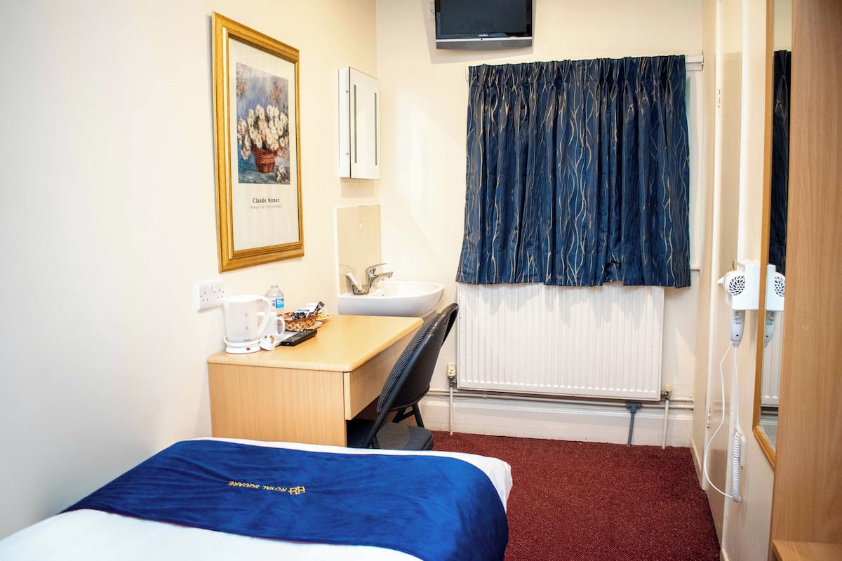 Une chambre d’hôtel comprenant un lit, un bureau avec une chaise, un lavabo, un miroir, un radiateur et un téléviseur fixé au mur.