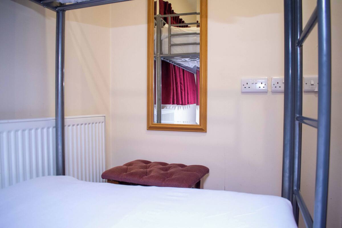 Un lit superposé avec une fenêtre, un radiateur et une prise électrique sur le mur.