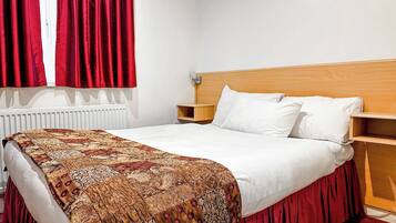 A neatly made bed with a patterned bedspread, a wooden headboard, and a red curtain.