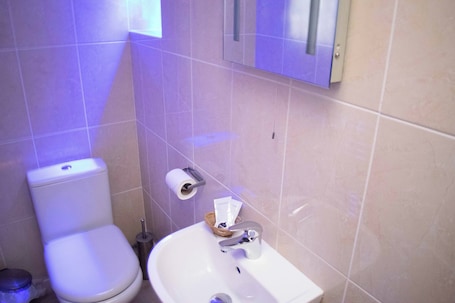 A bathroom with a toilet, sink, and a mirror.. Royal Square Hotel - NEC and Birmingham Airport