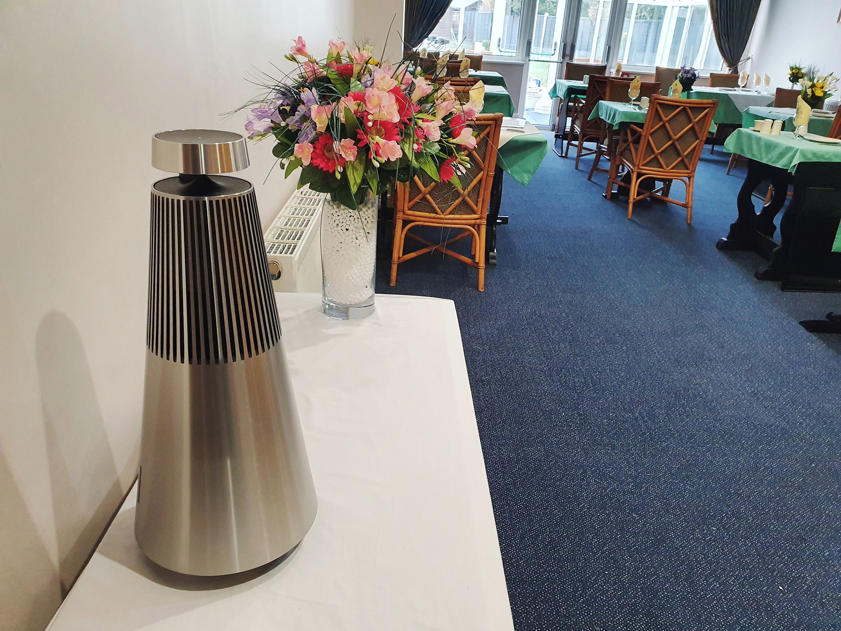 Ett rum med ett bord, en dekorativ vas med blommor och ett högt, cylindriskt föremål.