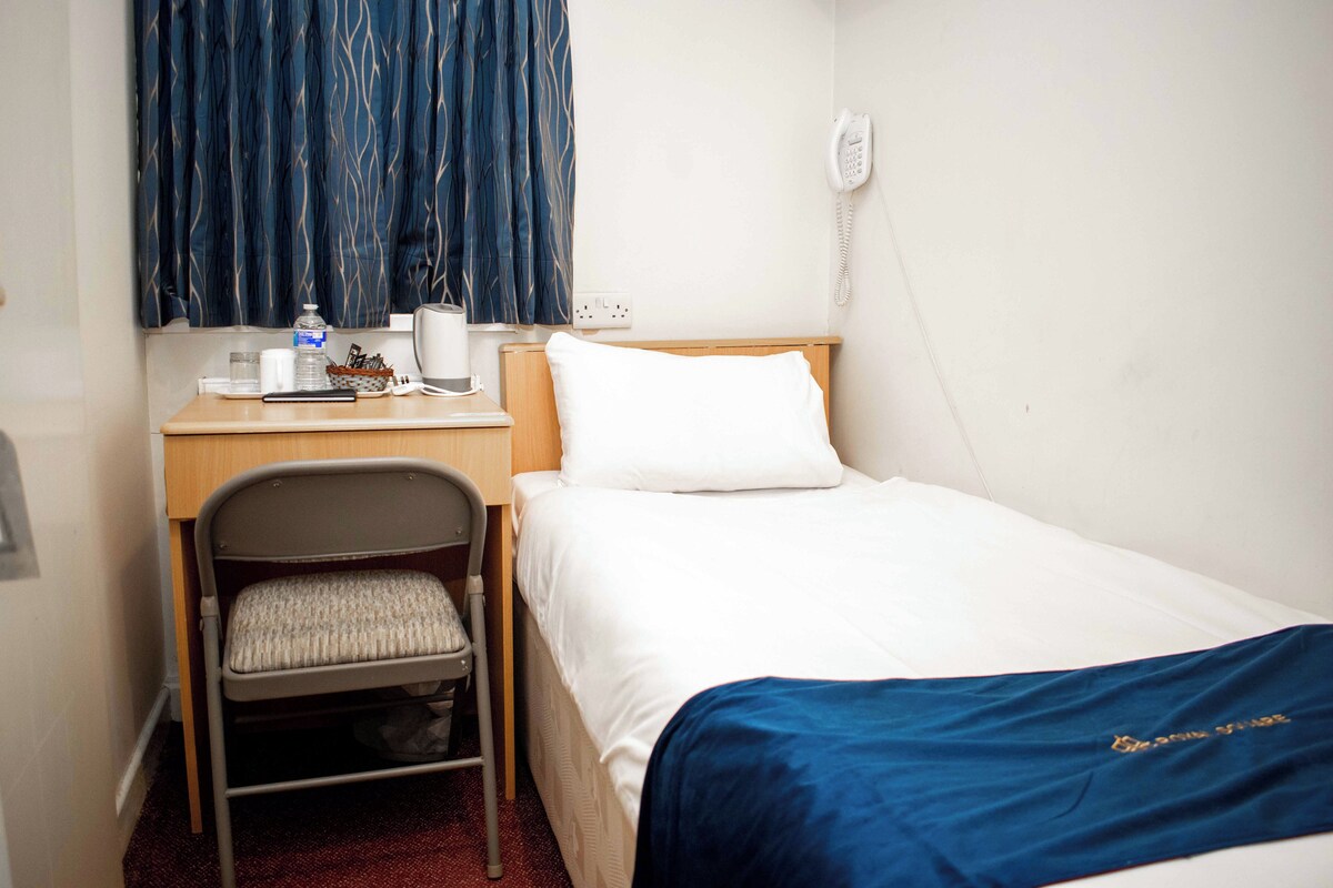 A hotel room with a bed, a desk with a chair, a telephone, and a window with curtains.