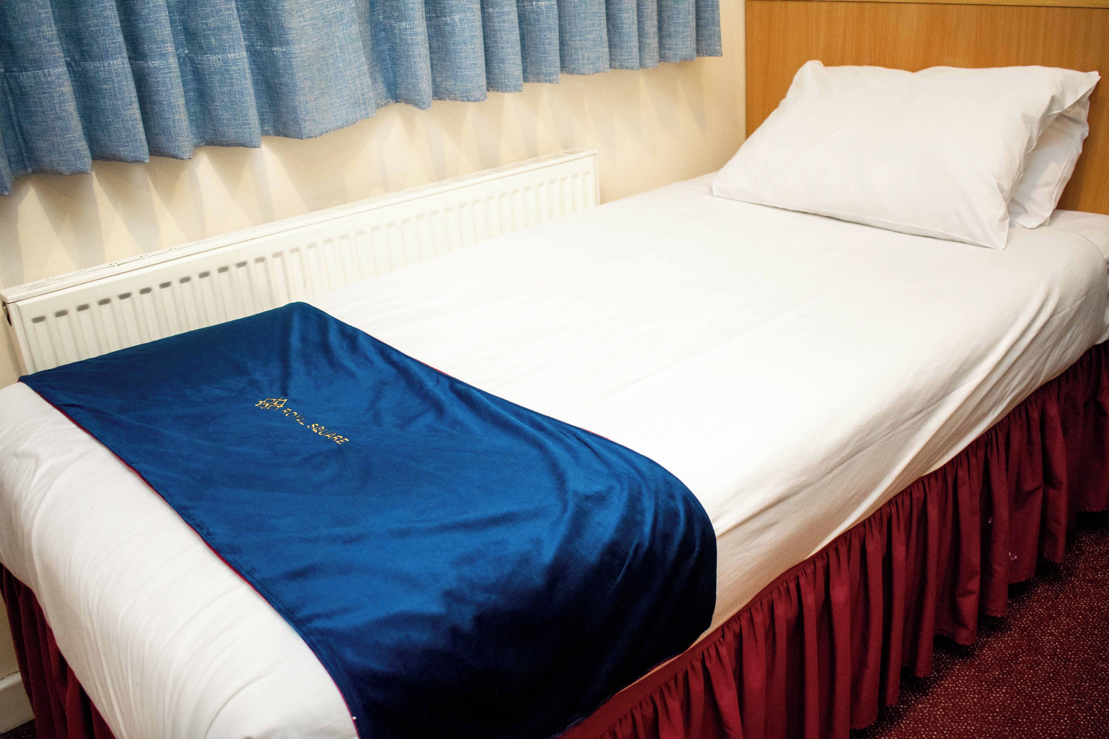 A bed with a white headboard, a blue blanket, and a red skirt.